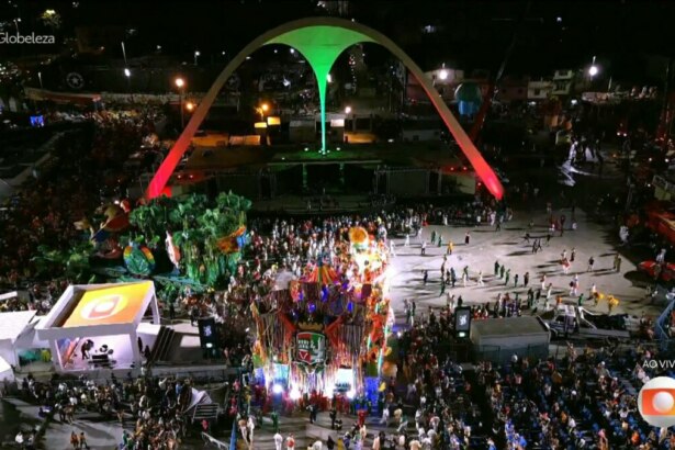 Imagem aérea noturna do Sambódromo do Rio de Janeiro durante um desfile de carnaval. A passarela está cheia de passistas e alegorias de uma escola de samba. As arquibancadas estão repletas de público. O icônico arco central está iluminado em vermelho e verde. A hashtag "#Globeleza" e o logo da Globo com a indicação "AO VIVO" são visíveis