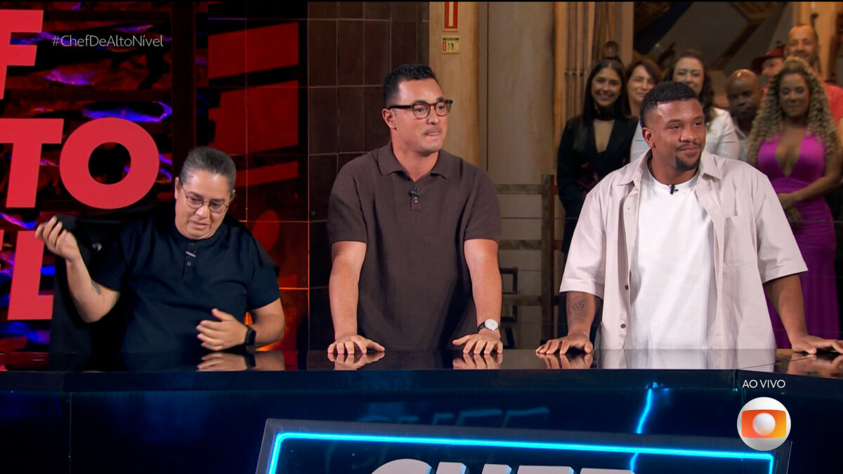 Três finalistas do reality "Chef de Alto Nível" — Luiz Lira, Arika Messa e Allan Mamede — estão lado a lado atrás de um balcão, sorrindo e aplaudindo durante a transmissão ao vivo da grande final