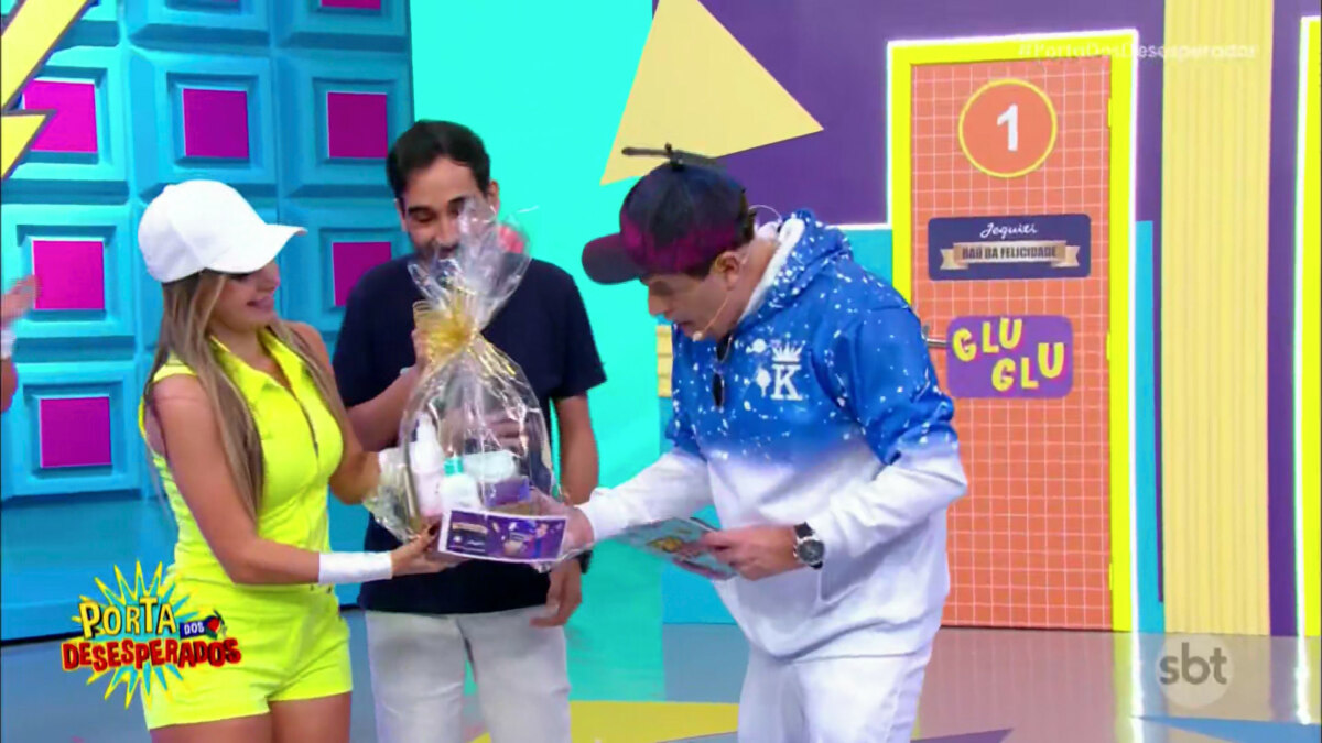 Sergio Mallandro observa carnê do Baú na cesta de presentes de um fã do SBT no palco do Porta dos Desesperados