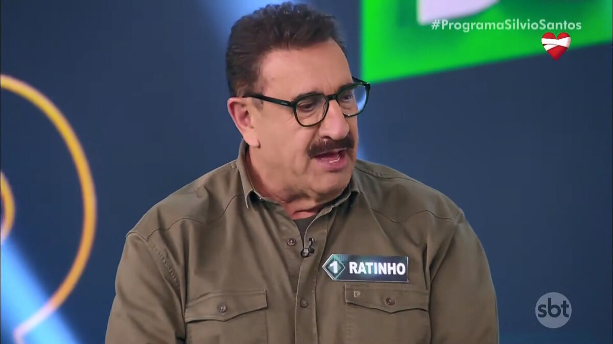 Apresentador Ratinho no palco do Programa Silvio Santos, usando camisa marrom com plaqueta de nome, durante participação no Show do Milhão Celebridades, onde declarou estar invicto na vice-liderança há 27 anos no SBT
