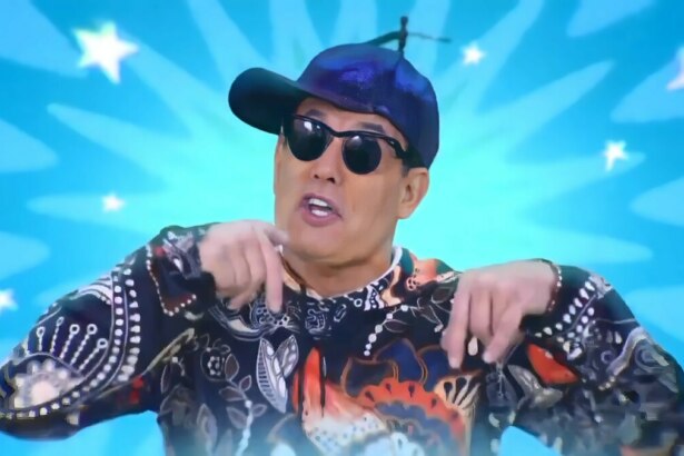Sérgio Mallandro no comercial do Porta dos Desesperados, usando boné azul e camisa colorida diante de fundo azul vibrante