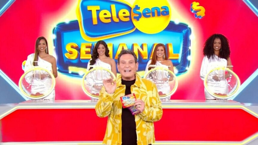 O apresentador Luís Ricardo no centro do palco, segurando uma Tele Sena, com quatro assistentes de palco de cada lado. O cenário é vermelho e amarelo com o logotipo "Tele Sena Semanal" em destaque. As assistentes de palco vestem blusas brancas de um ombro só e estão ao lado de globos de sorteio