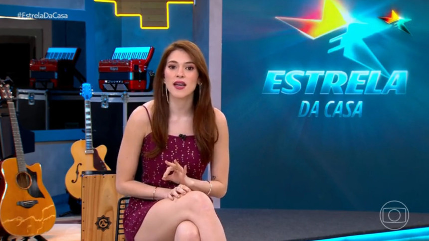 Ana Clara sentada em frente ao telão no cenário do Estrela da Casa