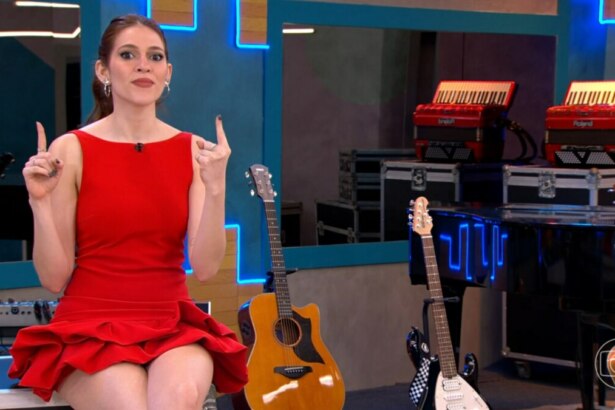 Ana Clara, de vestido vermelho, em um estúdio musical com guitarras e acordeões ao fundo no Estrela da Casa