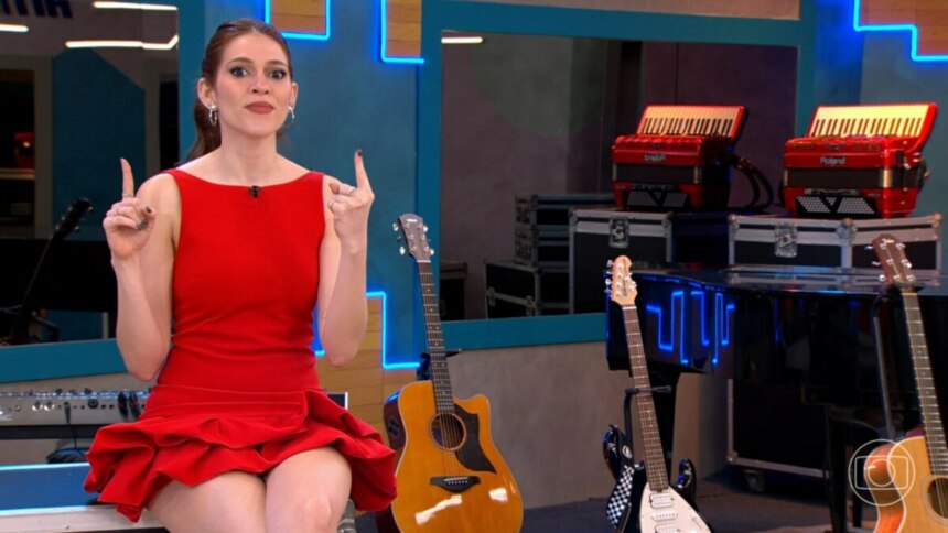 Ana Clara, de vestido vermelho, em um estúdio musical com guitarras e acordeões ao fundo no Estrela da Casa