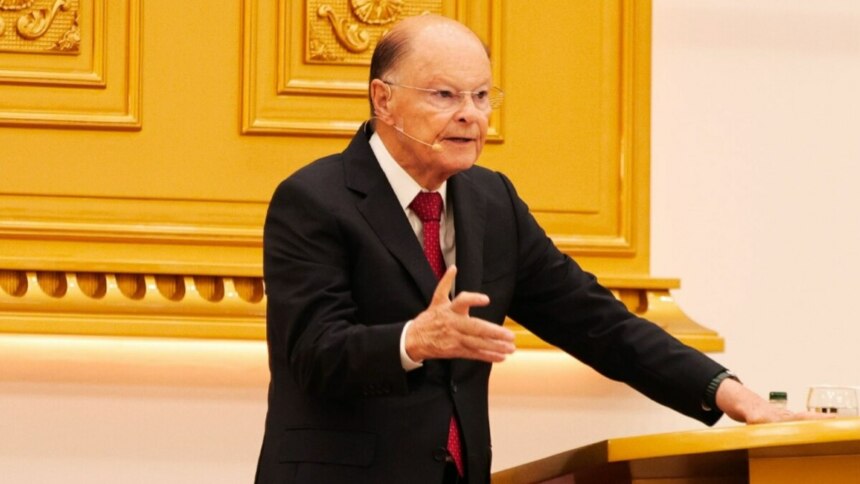Bispo Edir Macedo, de terno preto e gravata vermelha, em pé atrás de um púlpito dourado, gesticulando com a mão direita em um culto da Igreja Universal do Reino de Deus.