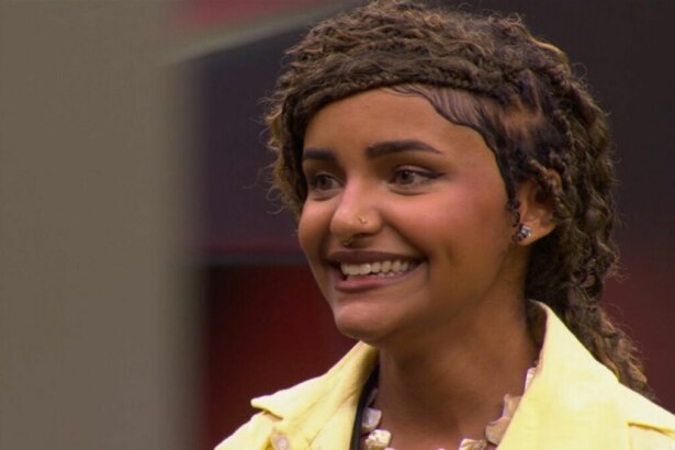Camille Vitória, de cabelos trançados, sorrindo e olhando para o lado, com uma jaqueta amarela em trecho da Prova do Jingle do programa Estrela da Casa.