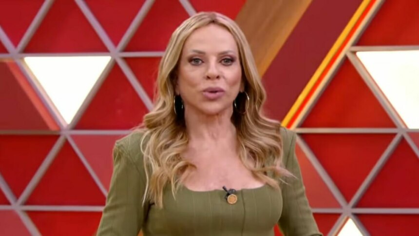 Christina Rocha de cabelos loiros e ondulados, usando uma blusa verde-militar, olhando diretamente para a câmera no cenário do programa Casos de Família.