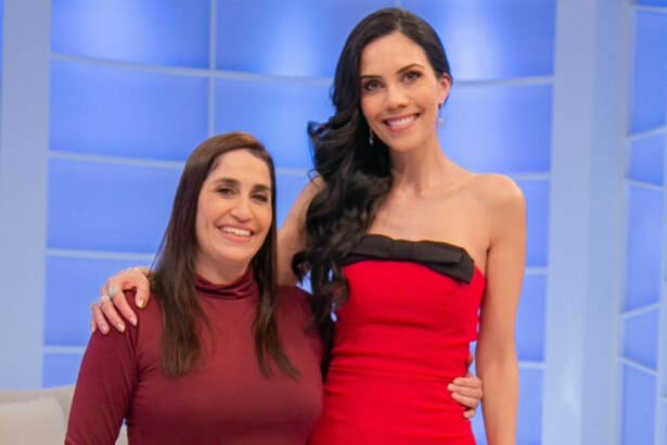 Daniele Hypolito e Daniela Albuquerque posando para a foto. Daniele, de blusa vinho, abraça Daniela, que usa um vestido vermelho tomara que caia com um laço preto na frente, no cenário do programa Sensacional.