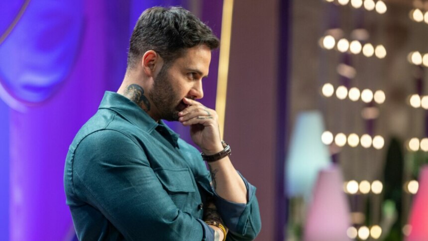 Diego Lozano, de camisa verde-azulada e com tatuagens visíveis no pescoço e braço, olhando pensativo para o lado com a mão no queixo, no cenário de MasterChef Confeitaria.