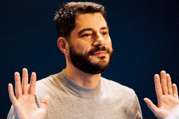 O jornalista Evaristo Costa, com barba e bigode, está com as mãos levantadas à altura dos ombros, com as palmas voltadas para a frente, em um gesto de "pare". Ele usa um suéter cinza-claro e olha para o lado.