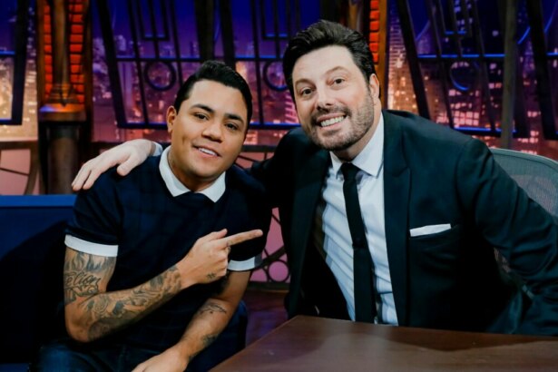 Felipe Araújo aponta para Danilo Gentili no cenário do The Noite, um retrato da dupla em um talk show.