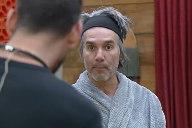 Fernando Sampaio, de roupão cinza e tiara, olha fixamente para outro participante, Nizam, durante uma discussão em A Fazenda.