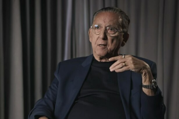 Galvão Bueno em entrevista, gesticulando com expressão séria, diante de cortinas em cenário intimista e iluminado.