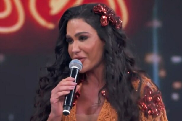 A musa fitness Gracyanne Barbosa chorando, segurando um microfone e com uma flor vermelha no cabelo, no palco do quadro Dança dos Famosos.