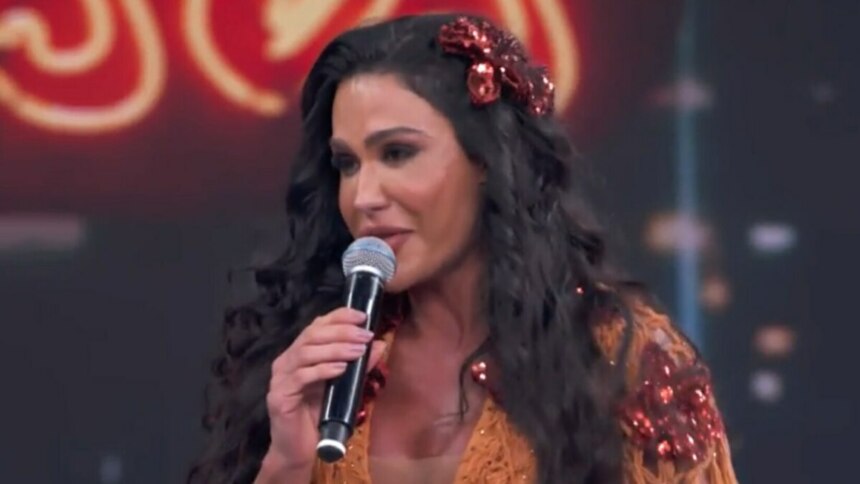 A musa fitness Gracyanne Barbosa chorando, segurando um microfone e com uma flor vermelha no cabelo, no palco do quadro Dança dos Famosos.