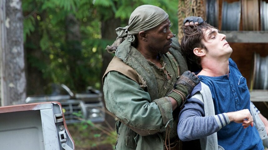Cena do filme Invasão Alienígena com o ator Wesley Snipes segurando outro homem pelo pescoço em uma floresta, com a caçamba de uma picape ao lado.