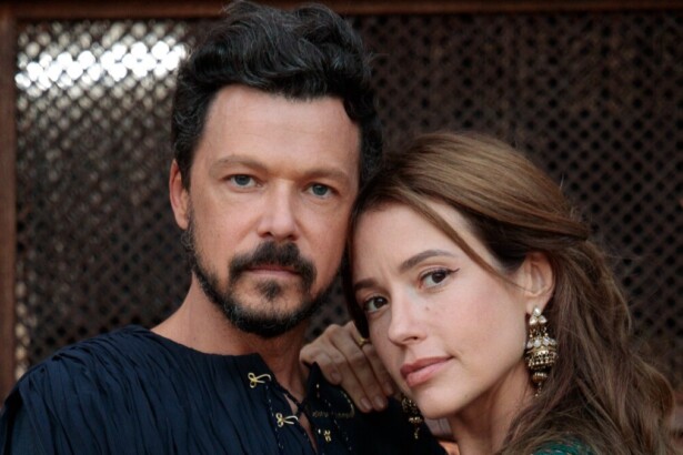 O ator Guilherme Berenguer, com barba e cabelos escuros, e a atriz Juliana Didone, com cabelo castanho claro e longos brincos dourados, posam juntos. A mão de Juliana está no ombro de Guilherme, em uma foto promocional da minissérie A Vida de Jó.
