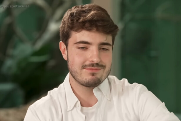 João Augusto Liberato, de barba, bigode e cabelos castanhos claros, usa uma camisa branca social e sorri de leve em uma entrevista para o programa Domingo Espetacular, com a hashtag do programa no canto superior da tela.