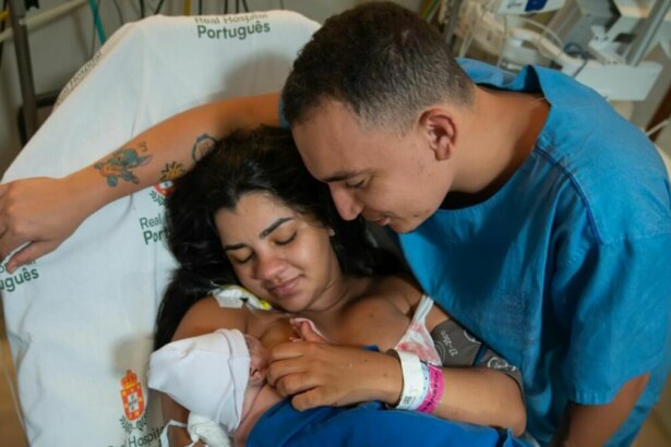 João Gomes e Ary Mirelle, emocionados, segurando o bebê recém-nascido no colo de Ary em um quarto de hospital.