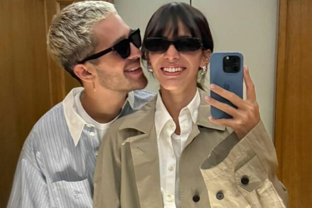 Bruna Marquezine e João Guilherme posando para uma selfie. Bruna está segurando o celular e sorrindo, enquanto João a abraça por trás e sorri, ambos usando óculos escuros.