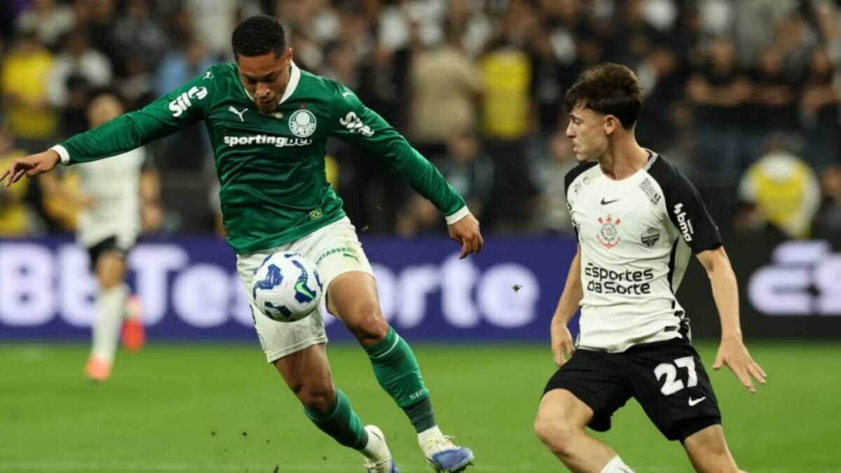 Jogador do Palmeiras, de camisa verde, chuta a bola enquanto jogador do Corinthians, de camisa branca, corre em sua direção, em partida do Brasileirão.