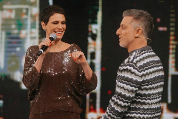 Malu Galli sorrindo e segurando microfone ao lado de Luciano Huck, ambos no palco do Domingão.