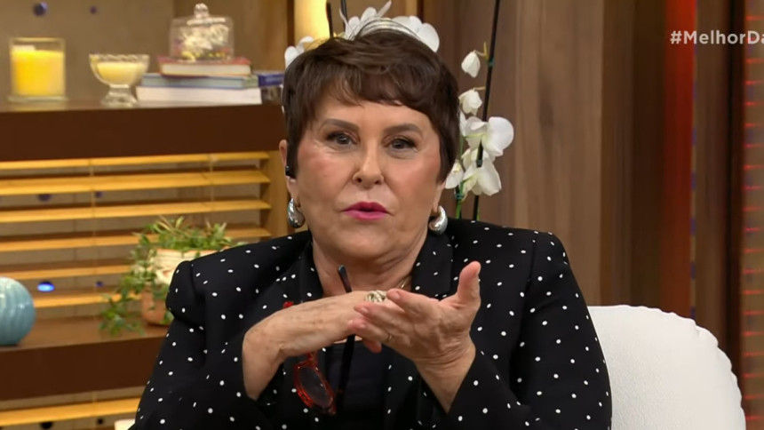 Marcia Sensitiva, com um blazer de bolinhas e brincos grandes, sorri e gesticula com as mãos, dando uma entrevista para o programa Melhor da Tarde.