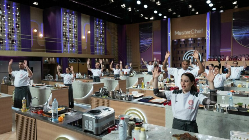 Os participantes do MasterChef Confeitaria em pé nas bancadas do estúdio, com as mãos levantadas para cima, celebrando a estreia do programa.