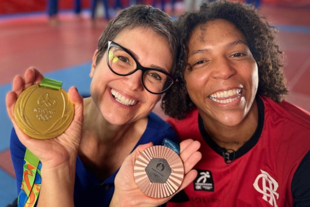A apresentadora Sandra Annenberg, de óculos, e a judoca Rafaela Silva posam sorrindo, segurando as medalhas olímpicas nos bastidores do programa Globo Repórter.