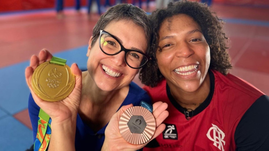 A apresentadora Sandra Annenberg, de óculos, e a judoca Rafaela Silva posam sorrindo, segurando as medalhas olímpicas nos bastidores do programa Globo Repórter.