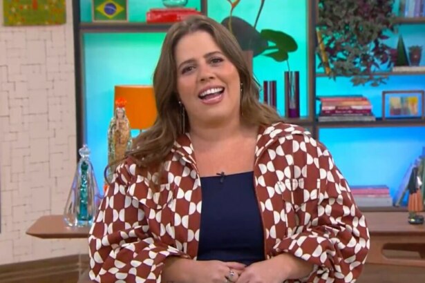 Tati Machado sorrindo para a câmera, usando uma jaqueta estampada e uma blusa azul-marinho, sentada no cenário colorido e aconchegante do programa Mais Você.