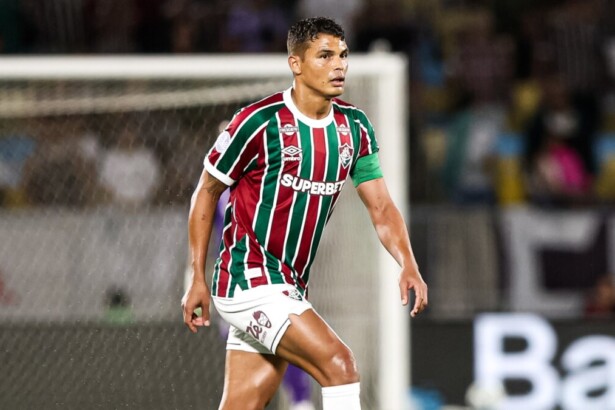 O jogador Thiago Silva, com o uniforme de listras verde, branca e grená do Fluminense, está no campo durante um jogo contra o Lanús pela Copa Sul-Americana, com uma expressão concentrada.