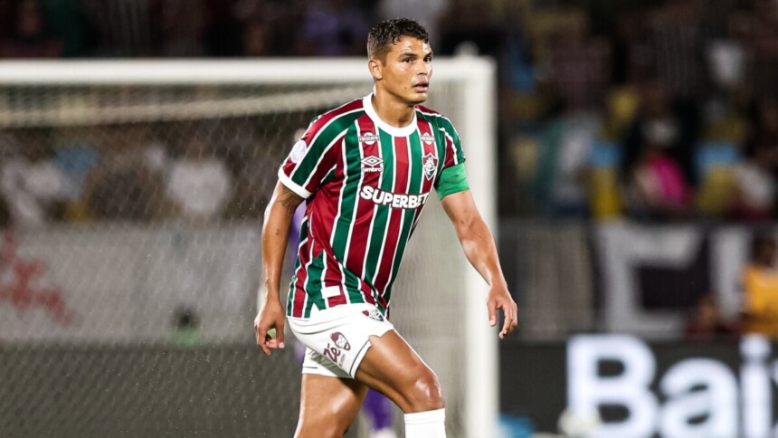 O jogador Thiago Silva, com o uniforme de listras verde, branca e grená do Fluminense, está no campo durante um jogo contra o Lanús pela Copa Sul-Americana, com uma expressão concentrada.