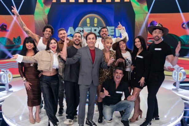 Tom Cavalcante com um terno cinza posa com os 12 participantes do reality show "Acerte ou Caia!" no palco, todos sorrindo e em clima de festa.