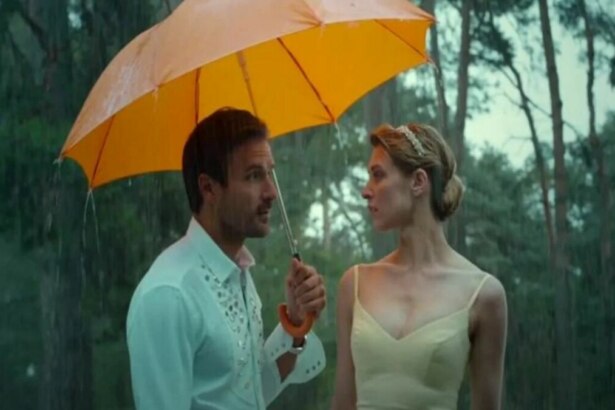Cena do filme Uma Noiva em Apuros. Um casal está na chuva, sob um guarda-chuva laranja. Eles se olham intensamente em um momento romântico.