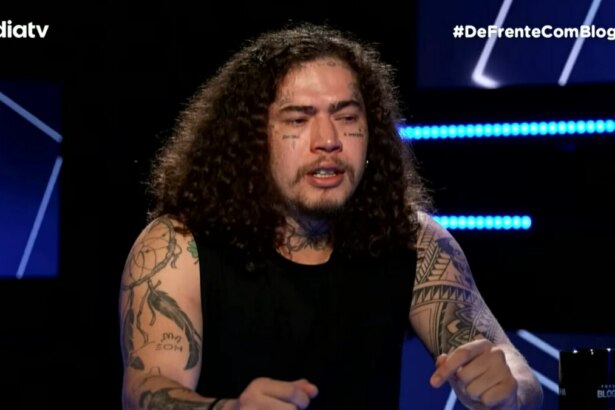 Whindersson Nunes, de cabelos cacheados e longos, com tatuagens no rosto e nos braços, olha para baixo e tem expressão emocionada no programa De Frente com Blogueirinha.