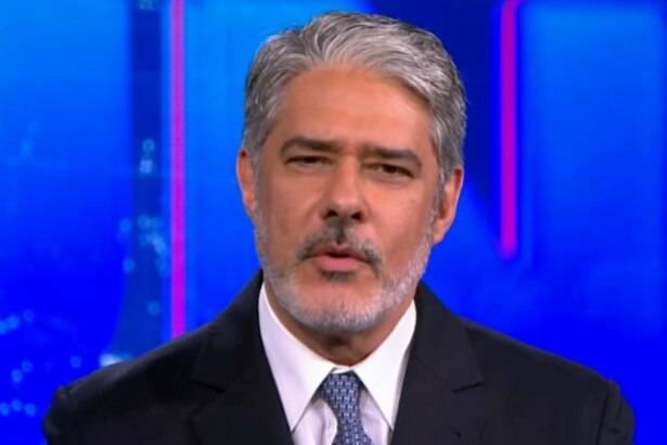 O jornalista William Bonner, com cabelos e barba grisalhos, está no estúdio do Jornal Nacional, usando terno e gravata, com expressão séria.