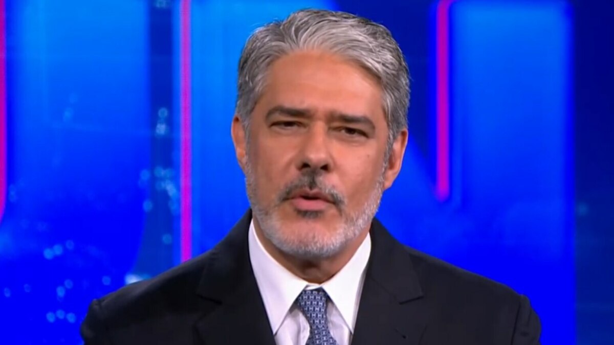 O jornalista William Bonner, com cabelos e barba grisalhos, está no estúdio do Jornal Nacional, usando terno e gravata, com expressão séria.