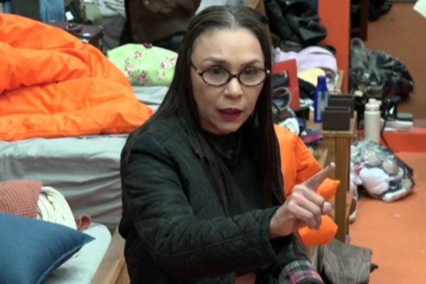 A influenciadora Yoná, de óculos e jaqueta preta, aponta para a câmera enquanto discute com alguém em um dos quartos do reality show A Fazenda.
