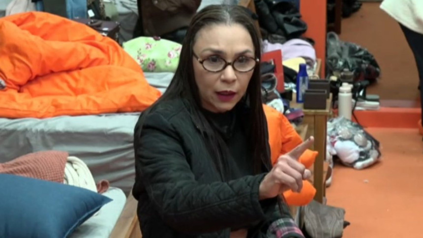 A influenciadora Yoná, de óculos e jaqueta preta, aponta para a câmera enquanto discute com alguém em um dos quartos do reality show A Fazenda.