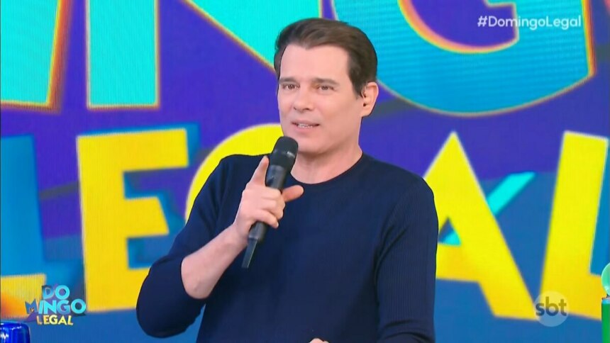 Celso Portiolli segura microfone do Domingo Legal e sorrir no palco do programa