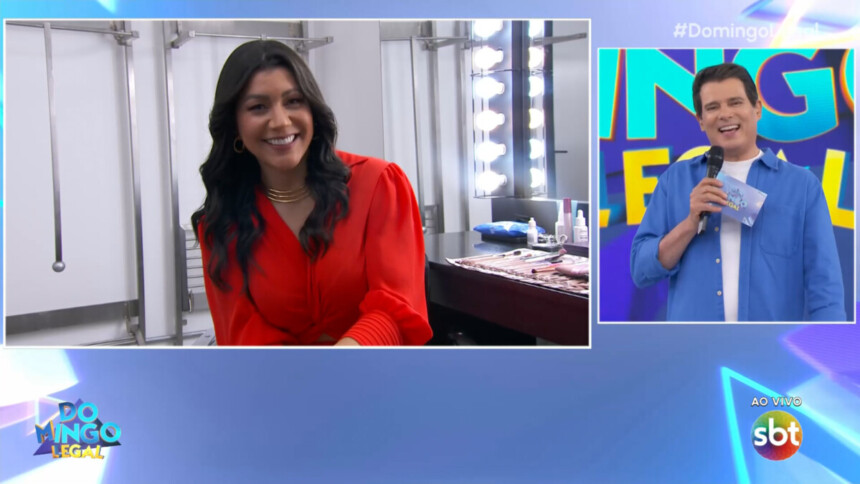 Dani Brandi, de blusa laranja, sentada no camarim do Domingo Legal conversando com Celso Portiolli que está no palco do SBT