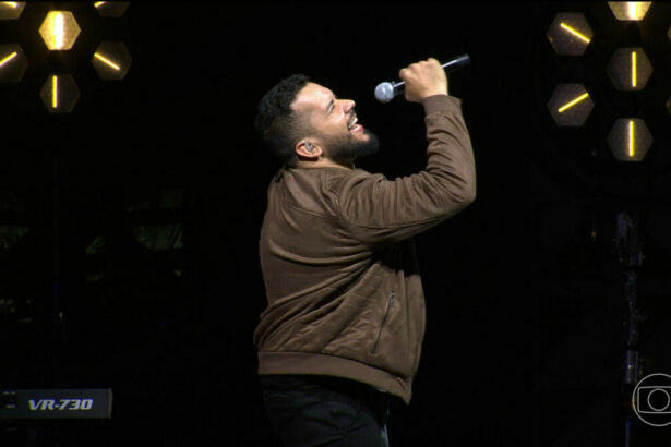 Janício segura o microfone como se fosse cantar no palco do Estrela da Casa 2