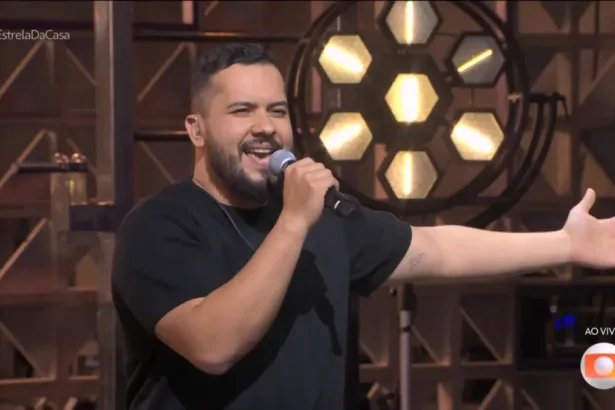 Janício, com o microfone na mão e abre o braço esquerdo, no Duelo no Estrela da Casa