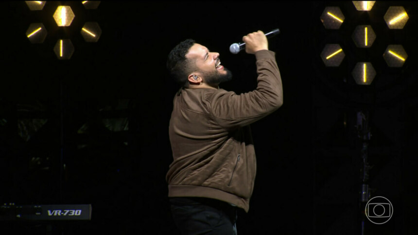 Janício segura o microfone como se fosse cantar no palco do Estrela da Casa 2