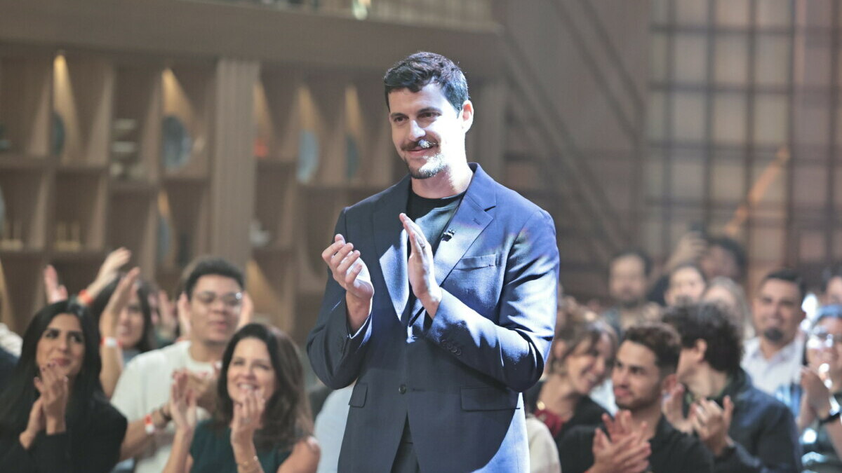 Felipe B. batendo palmas no centro do cenário do MasterChef Brasil 2025. Atrás dele um aplateia também bate palmas