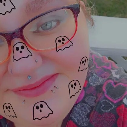 Seana com óculos e piercings, usando filtro de fantasmas no rosto, em ambiente externo com roupa colorida.