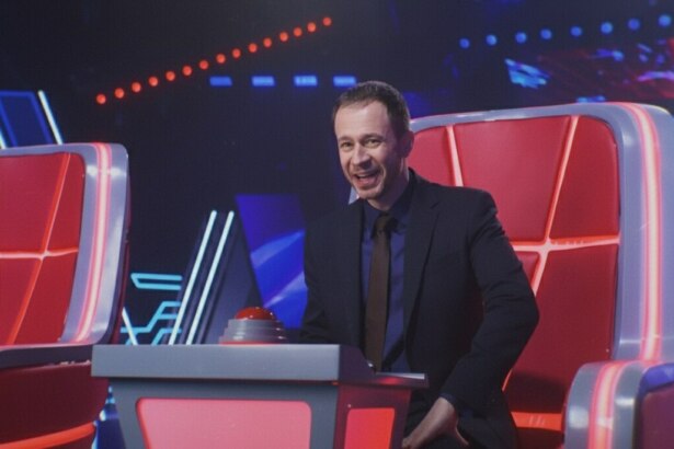 Tiago Leifert sentado em uma cadeira do The Voice Brasil 2025 e sorridente