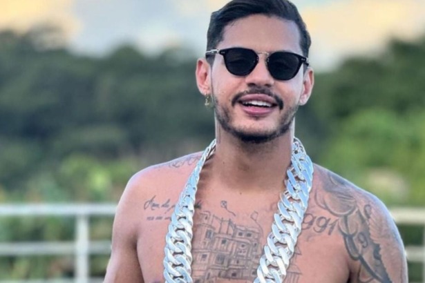 Rapper Hungria sem camisa, de óculos escuros e um colar prateado grosso. Ele tem barba e exibe tatuagens no peito.
